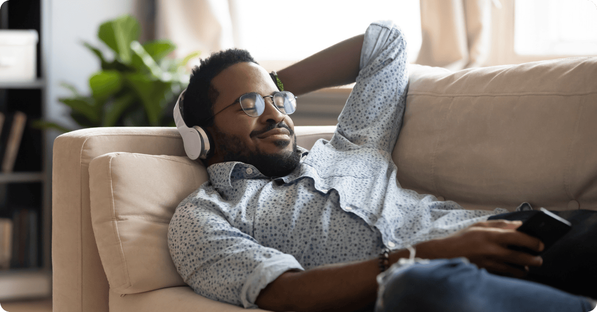 Man Enjoying an Online Hypnotherapy Session with Headphones on a Sofa